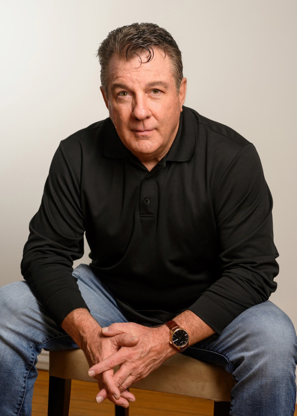 Here's an alt tag for the image: Man in black shirt, sitting.