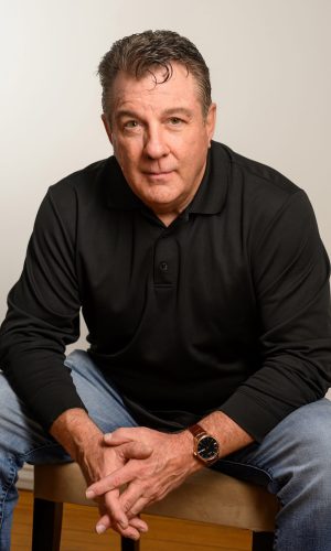 A man sitting on the ground wearing jeans and black shirt.